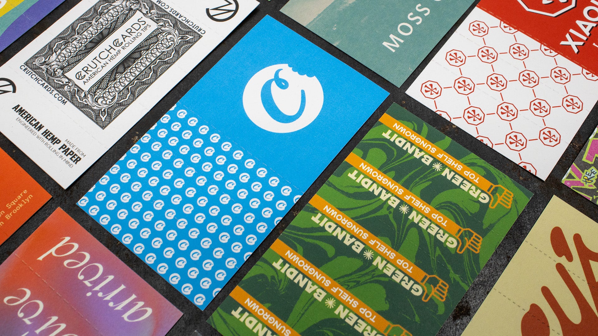 A flat lay of custom Crutch Cards featuring bold designs and branding, printed on hemp paper and arranged on a dark tabletop surface.