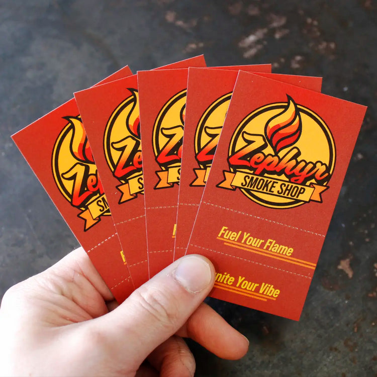 Hand holding a fanned-out set of five red Crutch Cards featuring the Zephyr Smoke Shop logo and slogan “Fuel Your Flame, Ignite Your Vibe,” with a dark textured background.