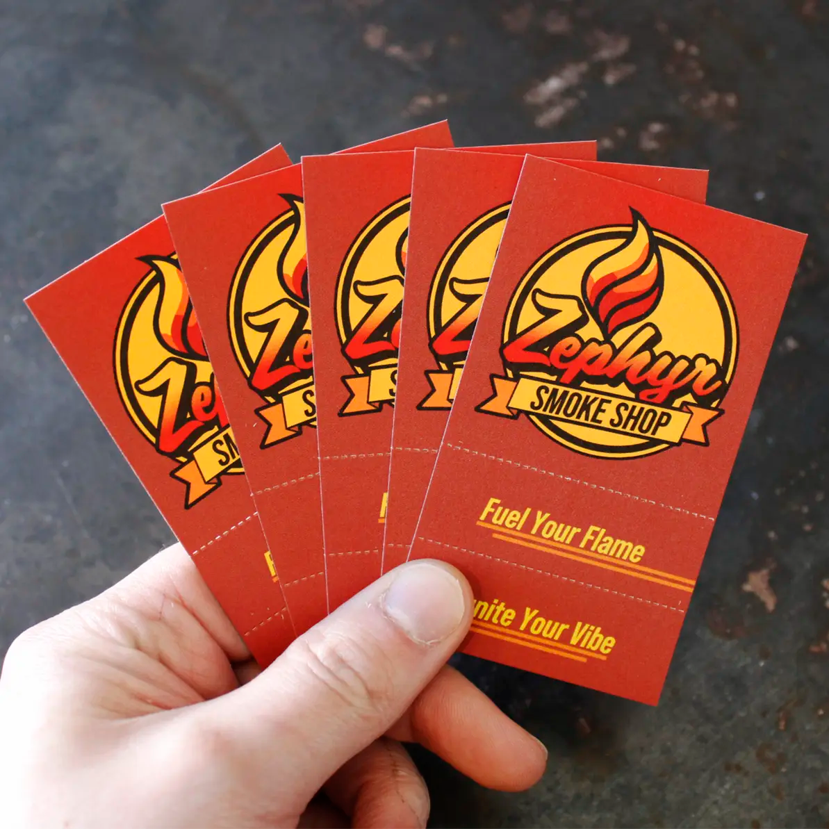 Hand holding a fanned-out set of five red Crutch Cards featuring the Zephyr Smoke Shop logo and slogan “Fuel Your Flame, Ignite Your Vibe,” with a dark textured background.