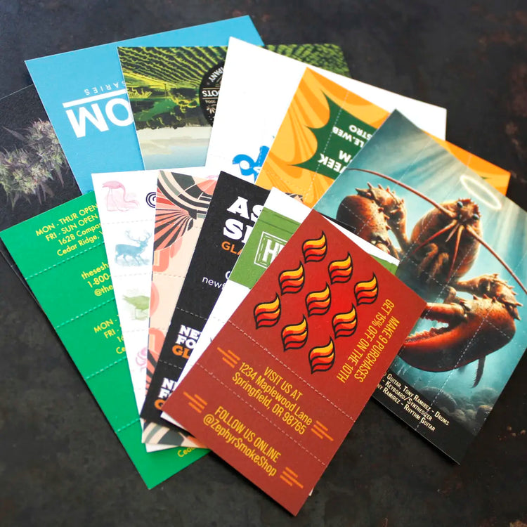 Spread of colorful Crutch Cards laid out on a dark surface, featuring diverse branded designs including graphics, logos, and business information, with visible perforations for rolling tips.