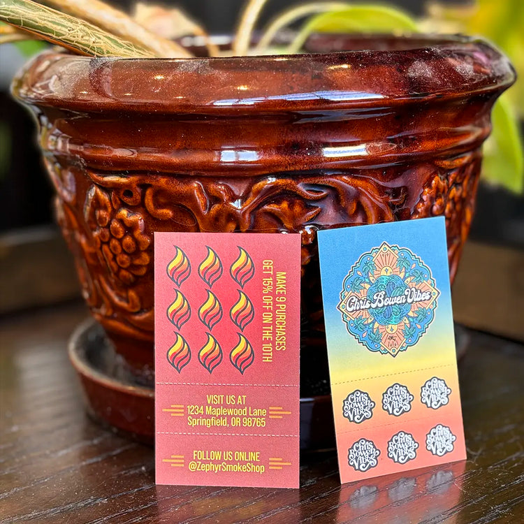 Two Crutch Cards propped up in front of a decorative ceramic planter—one with Zephyr Smoke Shop branding, the other with Chris Bowen Vibes artwork.
