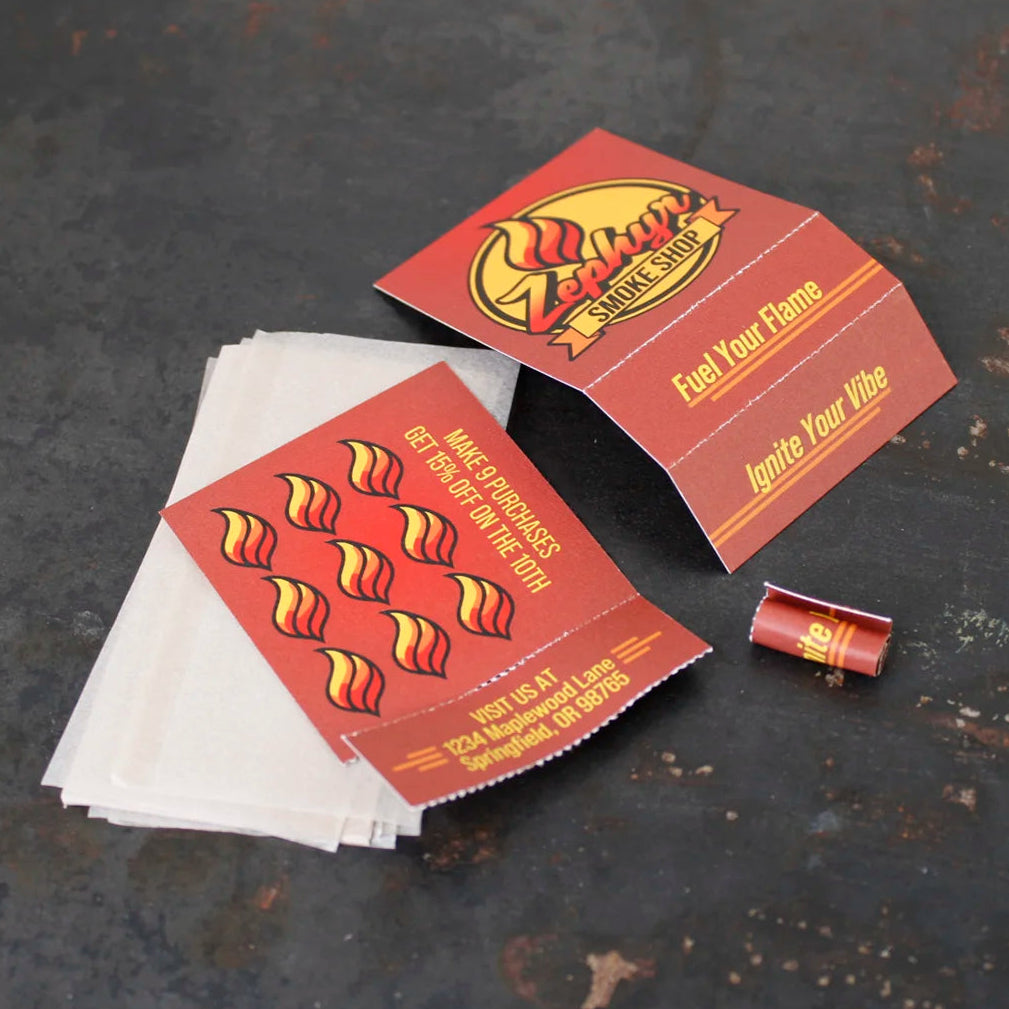 Crutch Cards for Zephyr Smoke Shop on a dark surface, featuring punch card-style design, branding, rolled tip, and stack of translucent hemp papers.