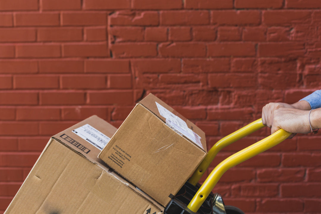 Person using a hand truck with cardboard boxes against a red brick wall